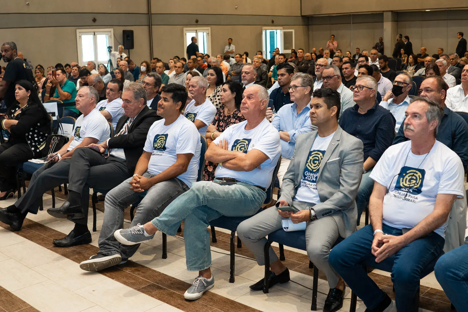 Auditório lotado durante workshop do Movimento Guarujá 2034, com integrantes vestindo camisetas do Movimento nas primeiras fileiras