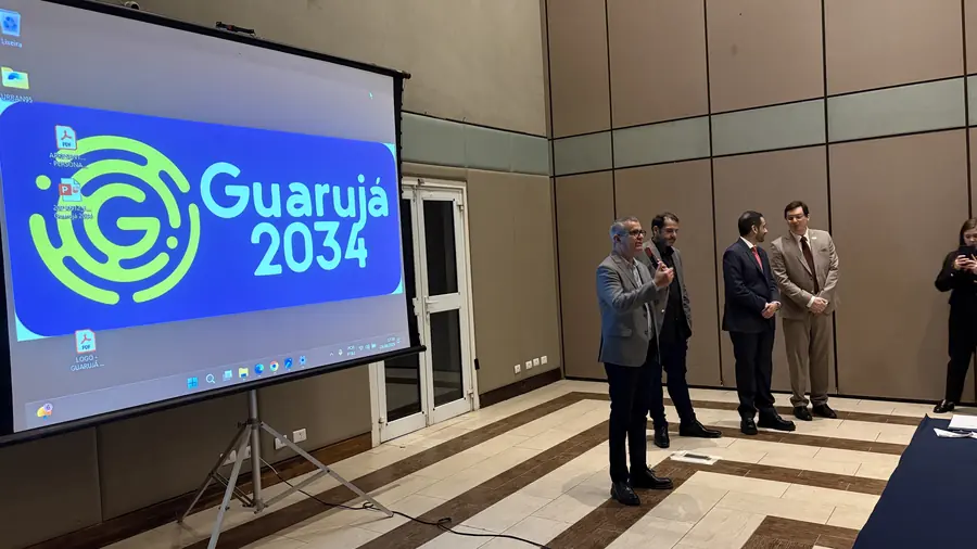 Participantes reunidos diante do telão com o logotipo do Guarujá 2034