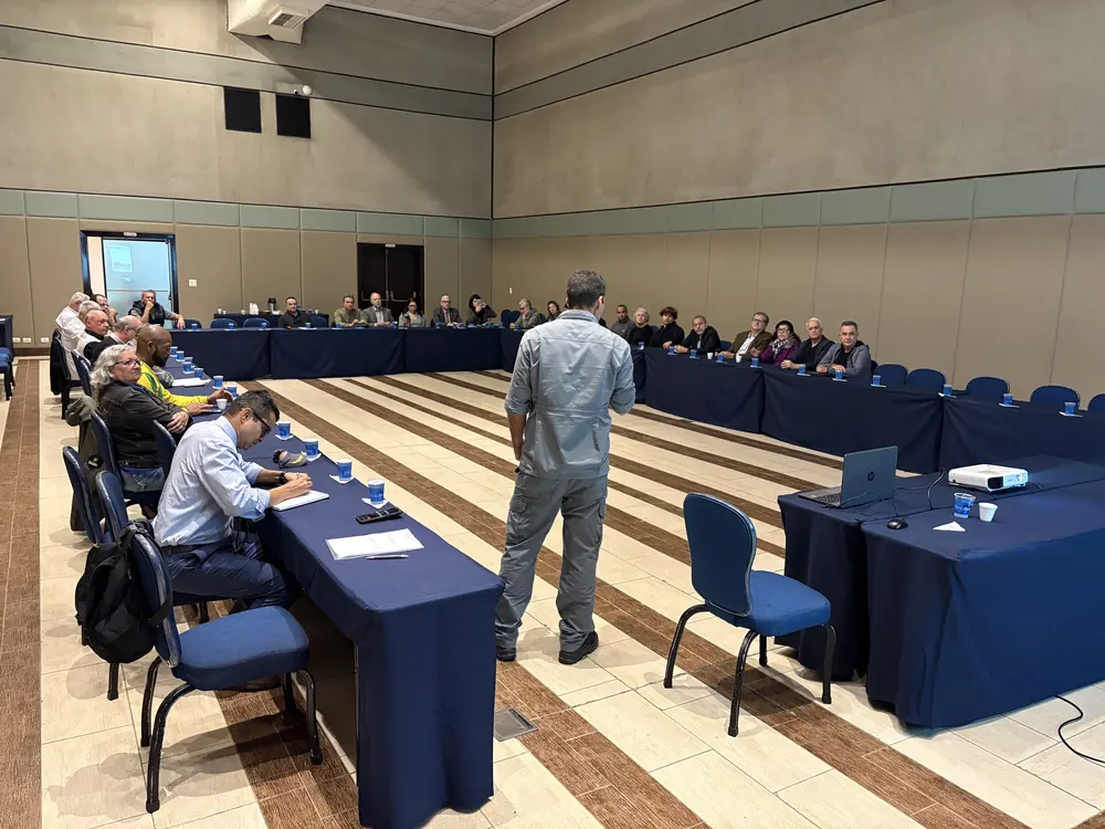 Reunião de trabalho do Movimento em sala com mesas em U e participantes acompanhando uma apresentação
